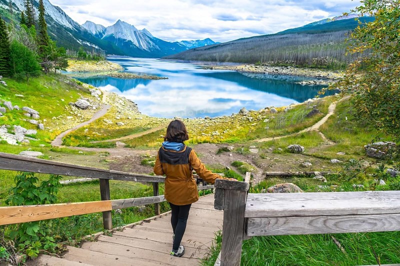 Female hiker descending wooden stairs towards the scenic medicine lake, surrounded by the canadian rockies in jasper national park, alberta, enjoying a peaceful moment in nature during a sunny day