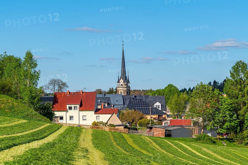 View across a mowed field to St. Lawrence Church and houses in the town of Elterlein, Ore Mountains, Saxony, Germany