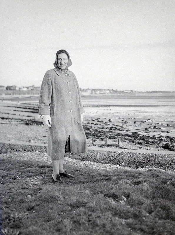 Full length portrait of smiling woman wearing winter coat and clothing standing by seaside, Devon, England, UKL c 1956