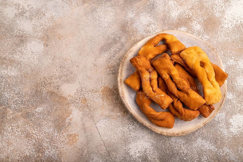 Crunchy biscuit Brushwood cookies sprinkled with powdered sugar on brown concrete background, top view, flat lay, copy space
