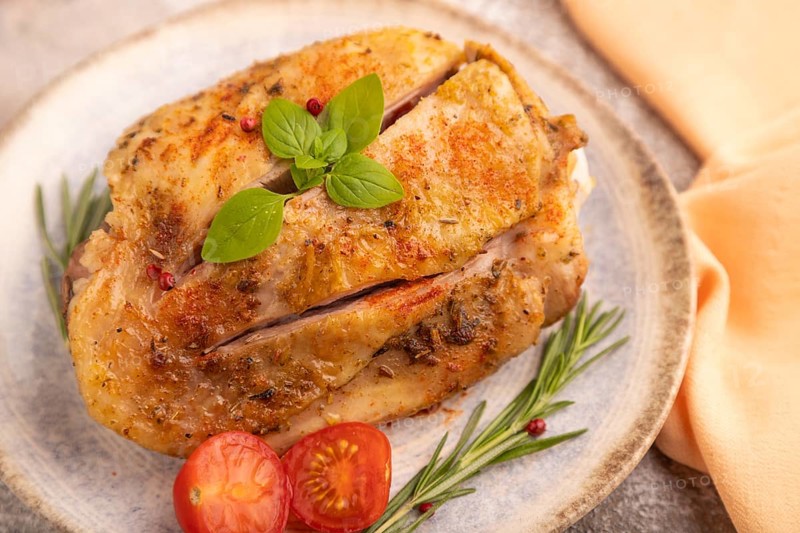 Fried Turkey Thigh with spices and rosemary on plate on brown concrete background and orange linen textile. side view, close up, selective focus