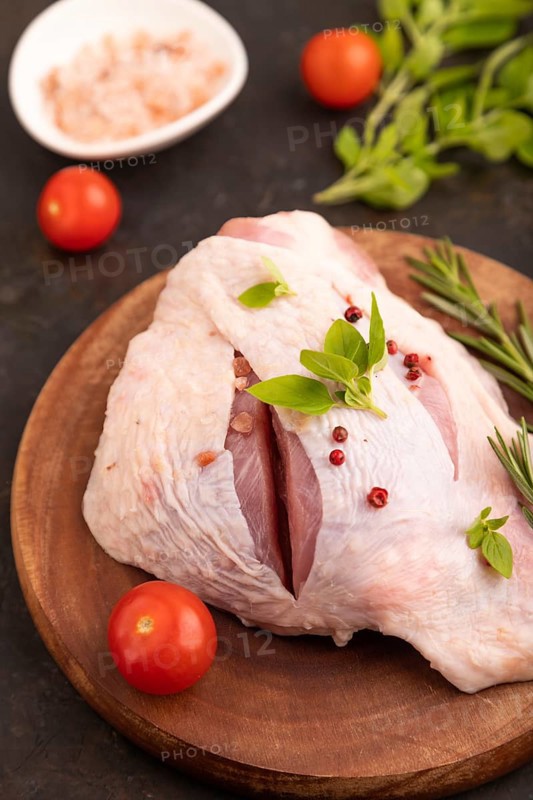 Raw Turkey Thigh with spices and rosemary on cutting board on black concrete background and linen textile. side view, close up, selective focus