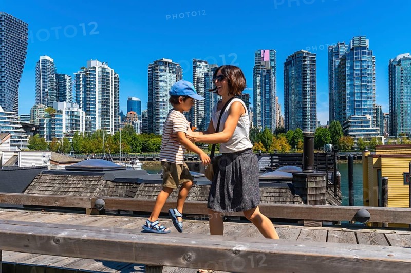 Mother and son enjoying a sunny day walking along the wooden boardwalk on granville island with the cityscape of vancouver, british columbia, canada, in the background