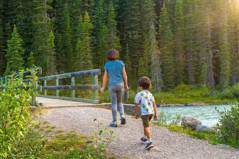Mother and son enjoying a leisurely hike along a scenic banff national park trail, surrounded by lush forests and a flowing river, capturing a heartwarming family moment in nature