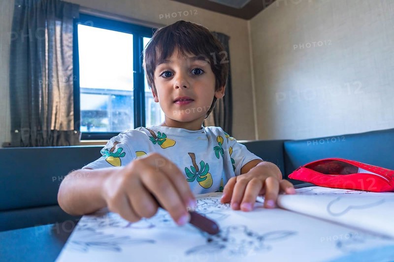 Young boy concentrating on drawing with crayons in a camper van, enjoying creative activities during a family vacation in banff national park, canadian rockies