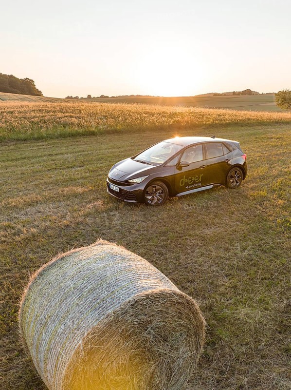 A black car is parked in a field next to a hay bale at sunset, deer e-car sharing, Cupra electric car, Black Forest, Germany