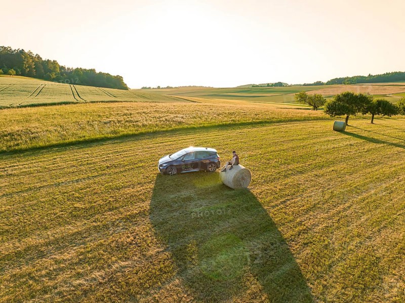 Car next to a hay bale in the middle of a vast golden field under the evening sun, deer e-car sharing, Cupra electric car, Gechingen, Germany