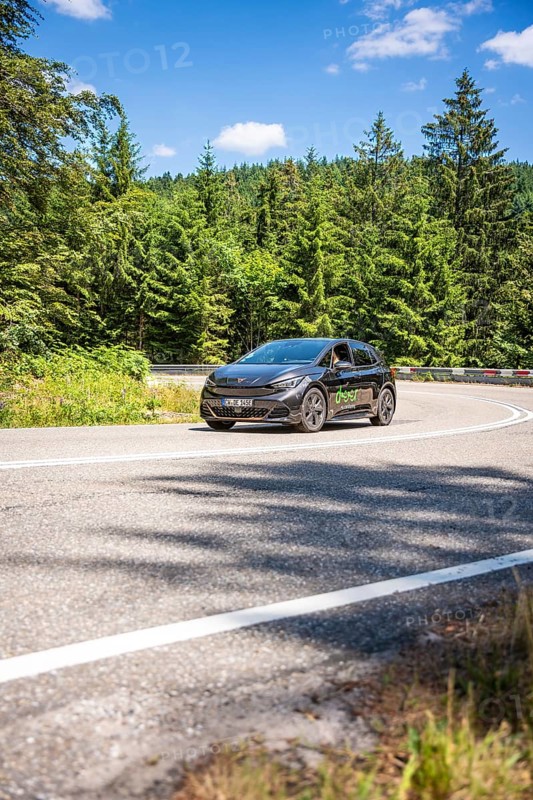 A black car drives on a winding road through a green forest on a sunny summer day, deer e-car sharing, Cupra electric car, Black Forest, Germany