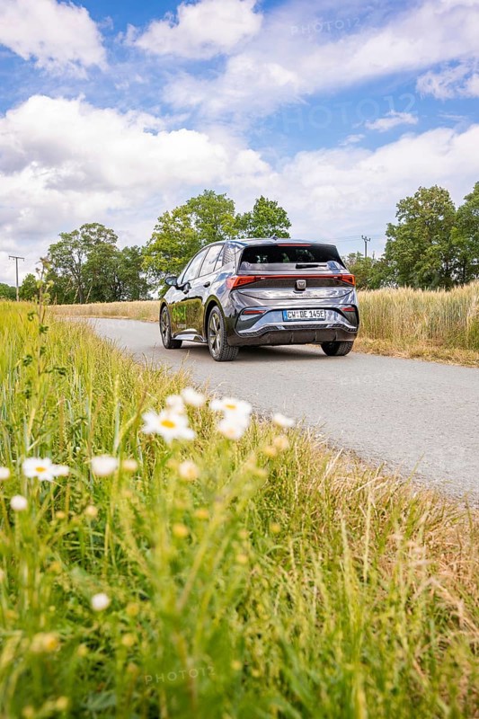 Black car driving on a country road with blooming meadows and cloudy sky, deer e-car sharing, Cupra electric car, Germany
