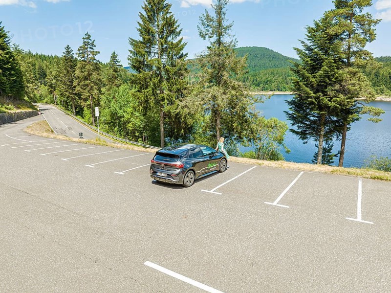 A car is parked near a lake, surrounded by forest and mountains on a clear day, deer e-car sharing, Cupra electric car, Black Forest, Germany