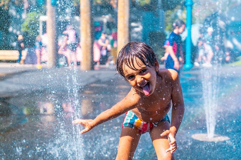 Happy child sticking out his tongue while playing in a water fountain on a sunny day in vancouver, british columbia, enjoying a playful moment of summer refreshment