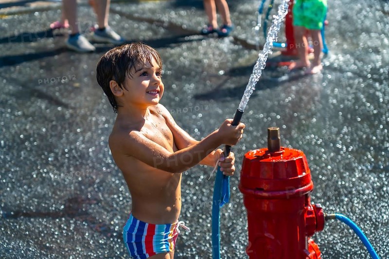 Smiling boy spraying water from a fire hydrant during a hot summer day in vancouver, british columbia, enjoying outdoor play and refreshment