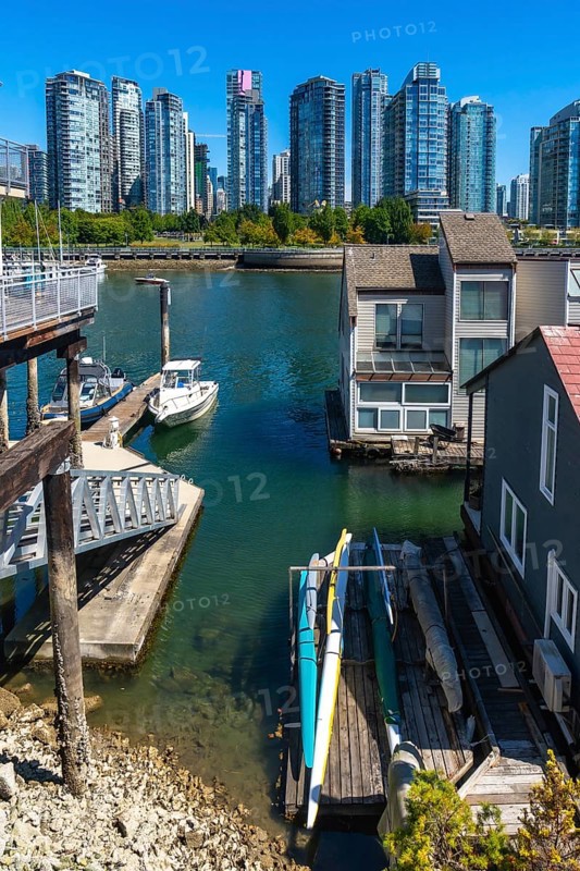 Kayaks resting on a wooden dock near floating homes, with a motorboat moored nearby and the vancouver skyline in the background, create a peaceful and scenic urban waterfront view