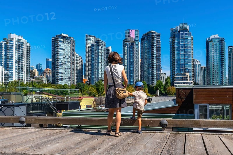 Mother and her son are enjoying the breathtaking view of the vancouver skyline, with its modern skyscrapers and vibrant cityscape, from the wooden deck of granville island market on a sunny day