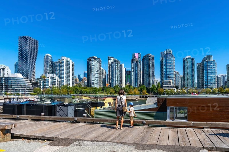 Mother and son standing on a wooden pier, admiring vancouver's modern skyline with high rise buildings and a clear blue sky from granville island market