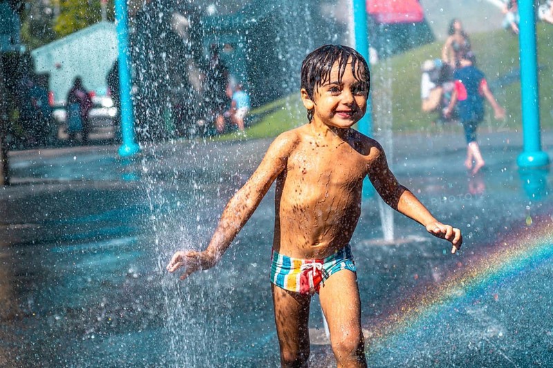 Happy muddy child playing and running through jets of water in a playground water park fountain in vancouver, british columbia, canada, enjoying summer vacation