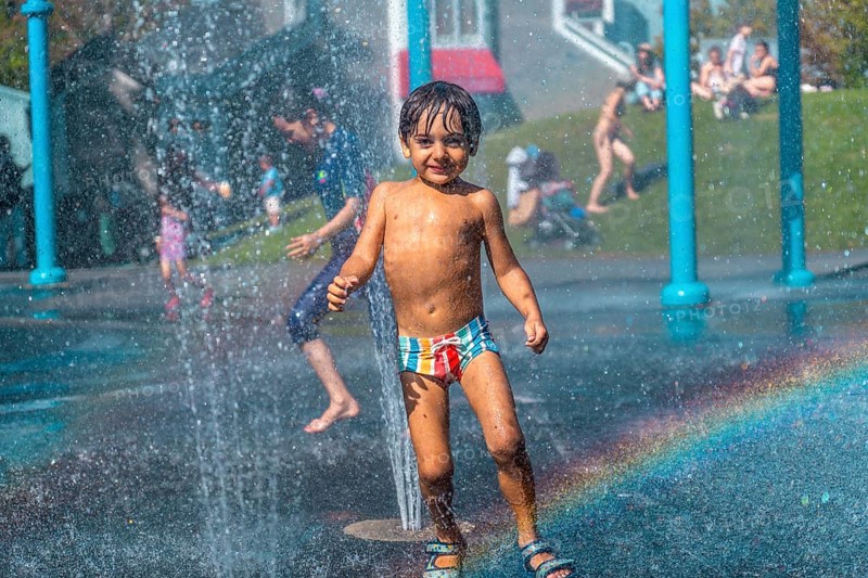 Happy child playing and running under the water jets of a splash pad in vancouver, british columbia, during a sunny summer day, creating a rainbow effect