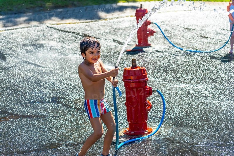Happy child playing and splashing with water jets coming out of a small red fire hydrant during a hot summer day in vancouver, british columbia