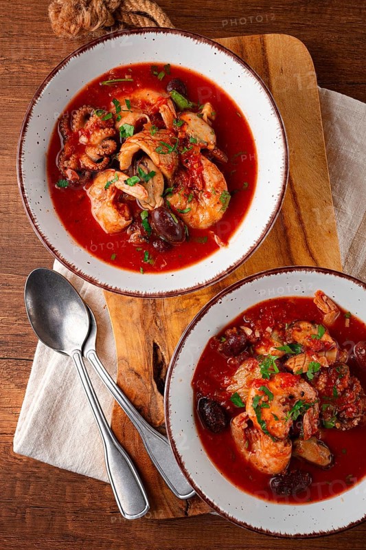 Two plates of seafood in tomato sauce, olives, top view