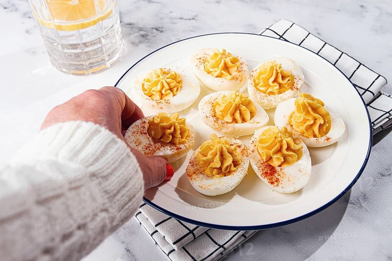 Stuffed eggs with paprika, on a plate, a woman's hand reaches for it
