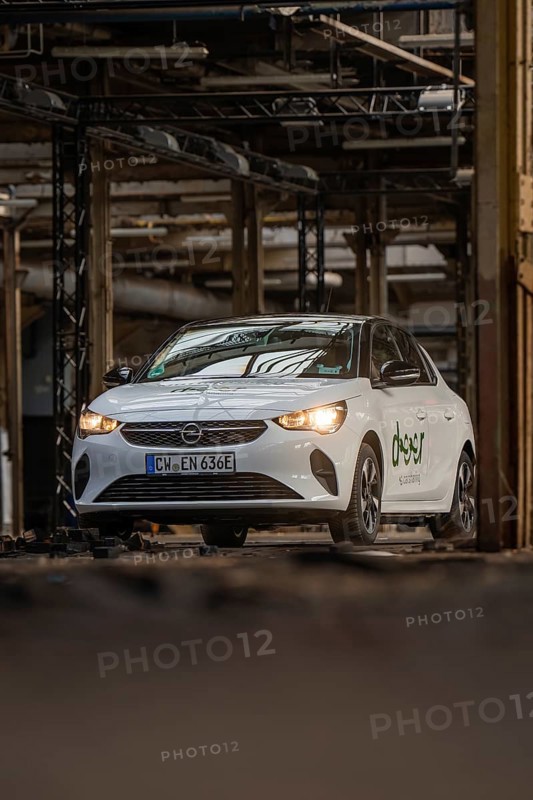 A white Opel with car sharing logo drives through an urban, industrial environment, Deer E-Car Sharing, Motorworld Rüsselsheim, Germany