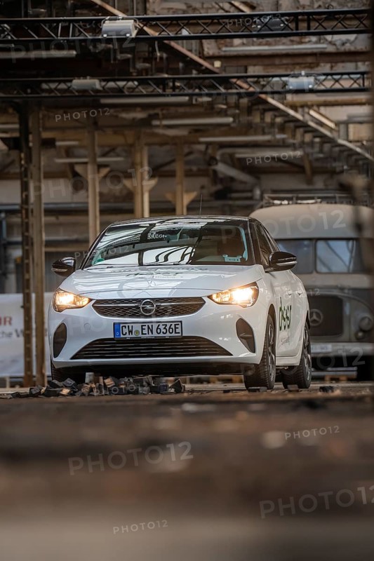 White Opel with car sharing logo in an urban industrial building with visible metal structures, Deer E-Car Sharing, Motorworld Rüsselsheim, Germany