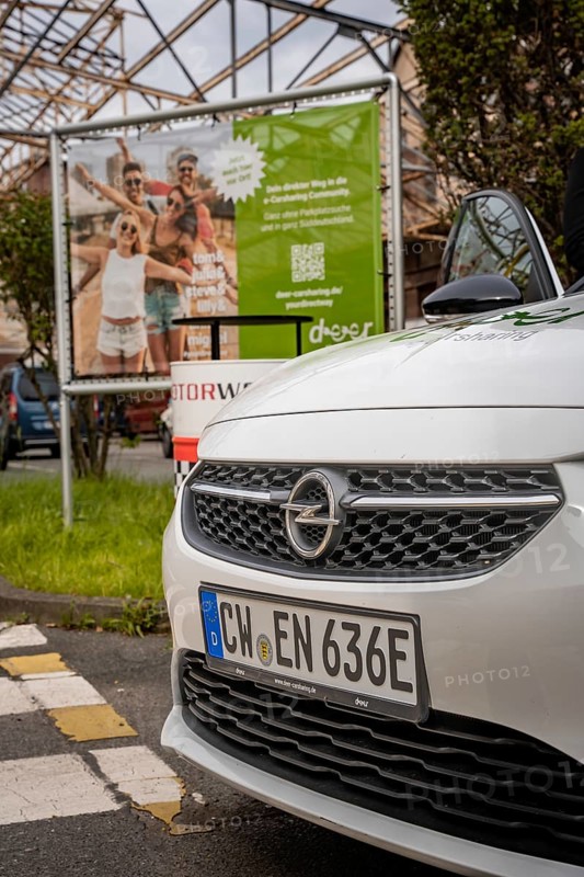 White Opel front in the foreground with car sharing advertising in the background, Deer E-Car Sharing, Motorworld Rüsselsheim, Germany