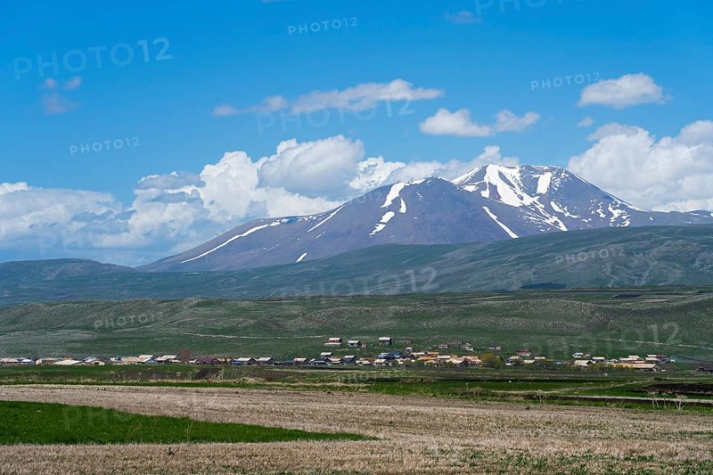 View of snow-capped mountains behind vast fields and a village, landscape near Satche, Mount Didi Abuli, Samtske-Javakheti region, Samtske Javacheti, Lesser Caucasus, Georgia