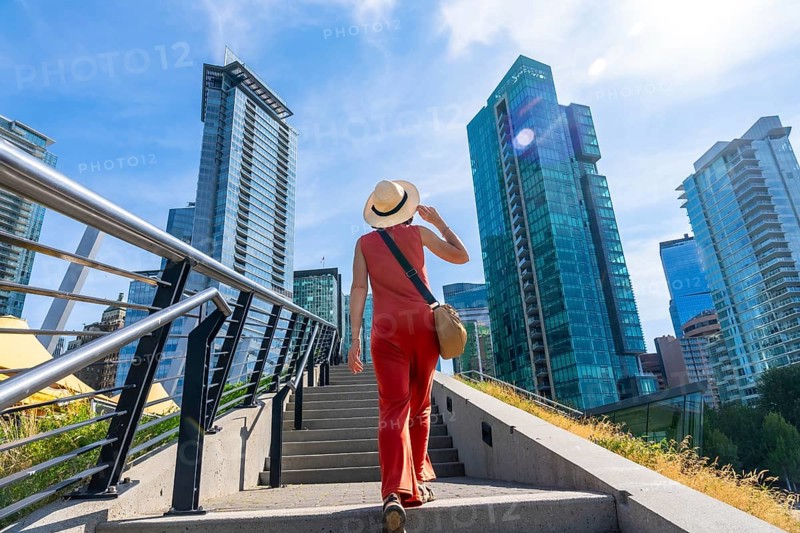 Tourist wearing a straw hat walking up stairs in vancouver, british columbia, canada with modern buildings and blue sky in background during sunny summer day