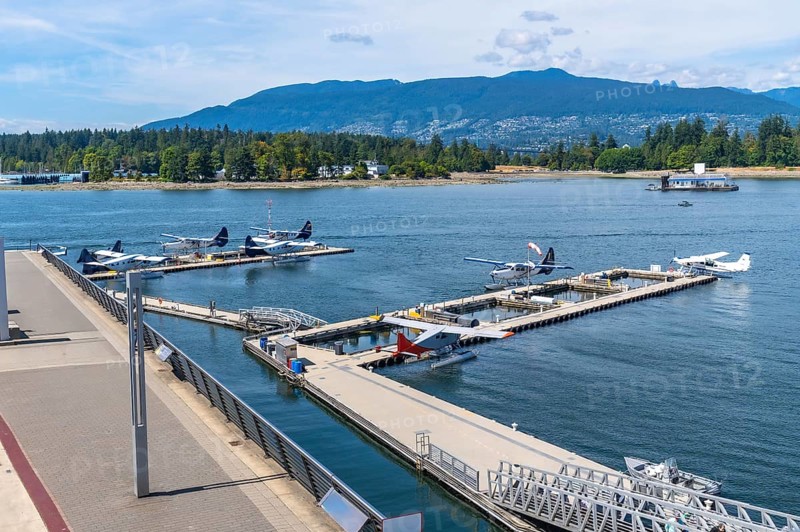 Seaplanes are docked in the harbor at coal harbour in vancouver, british columbia, canada, with stanley park and the north shore mountains in the background on a sunny summer day