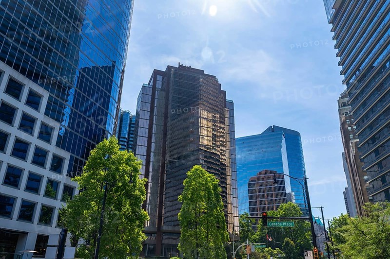 Sunlight illuminates the modern skyscrapers and lush green trees of vancouver's financial district, showcasing the city's vibrant urban landscape on a clear day