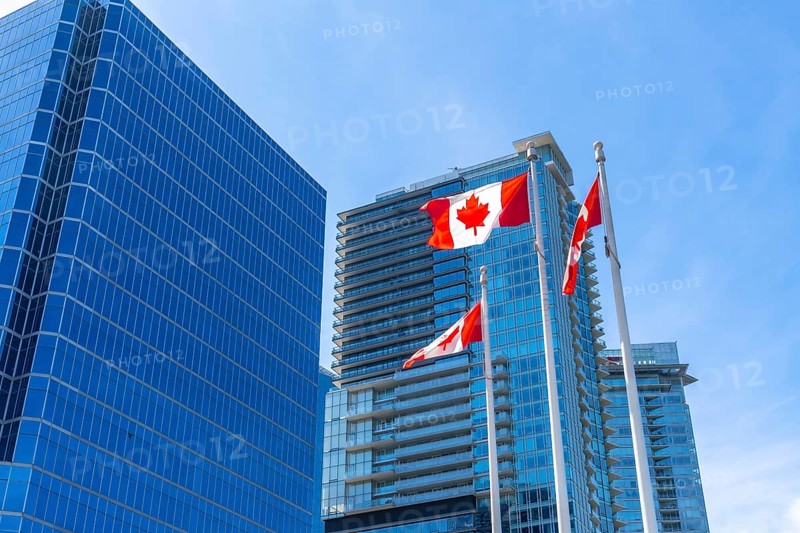 Three canadian flags are waving proudly against a backdrop of modern skyscrapers in downtown vancouver, british columbia, symbolizing national pride and urban progress
