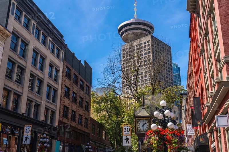 Gastown steam clock with flower decorations rising towards harbour centre, a skyscraper located in downtown vancouver, british columbia, canada, on a beautiful summer day