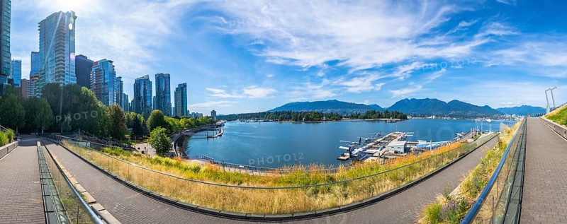 Panoramic view of vancouver's modern skyline rising above a picturesque waterfront, showcasing lush parks, calm blue waters, and boats swaying on a sunny day