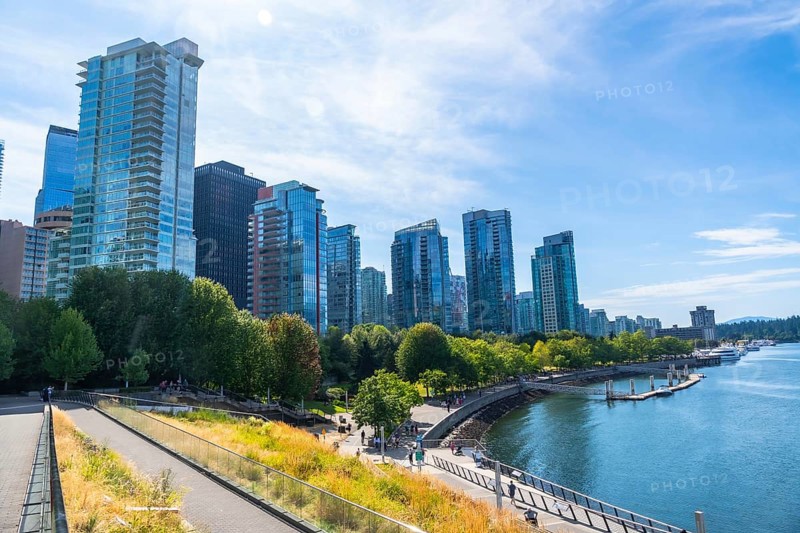 Vancouver's modern cityscape rises above a vibrant waterfront park, showcasing a blend of urban development and natural beauty on a clear, sunny day