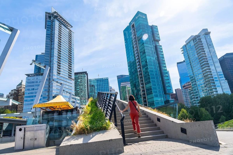 Woman is climbing the stairs of a pedestrian overpass with modern skyscrapers and a clear blue sky in the background in vancouver, canada