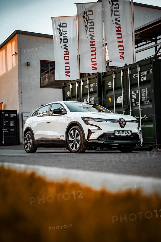 White electric car in front of a Motorworld building with flags and containers, Deer e-Carsharing, Renault Megane, Calw, Germany