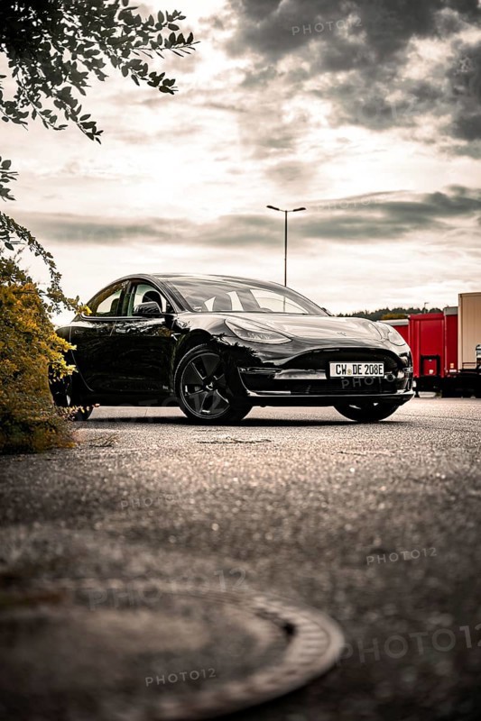 Black car in a parking lot under cloudy sky with trees nearby, Deer E- car sharing, Tesla Model 3, Calw, Germany