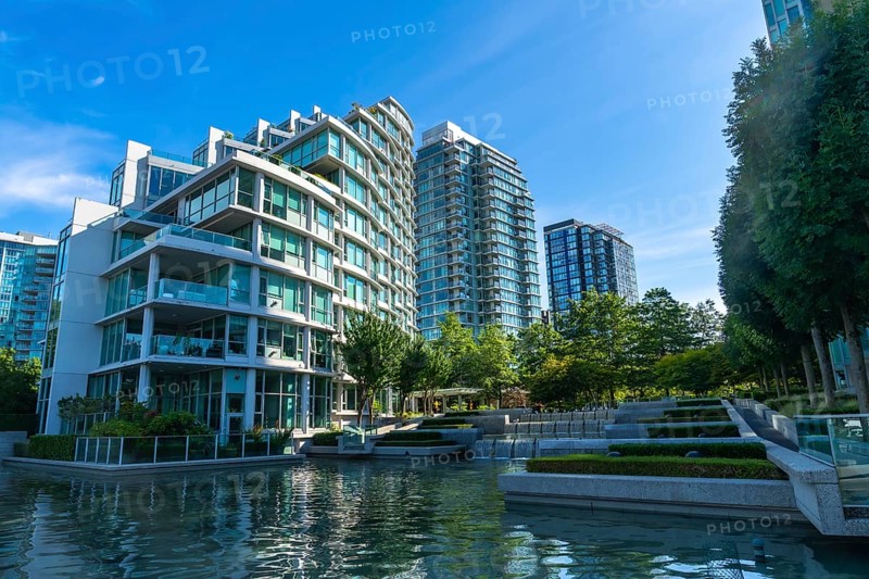 Modern glass and concrete buildings stand tall, reflecting in the calm water of a city park, creating a serene urban oasis in vancouver, british columbia
