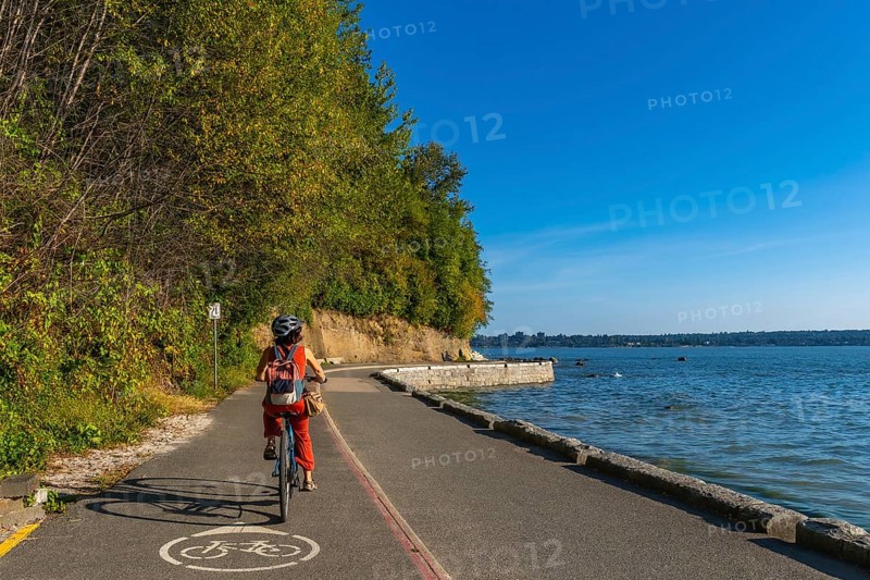 Tourist cycling through stanley park, soaking in stunning ocean views and vibrant cityscapes on a sunny summer day in vancouver, british columbia, canada