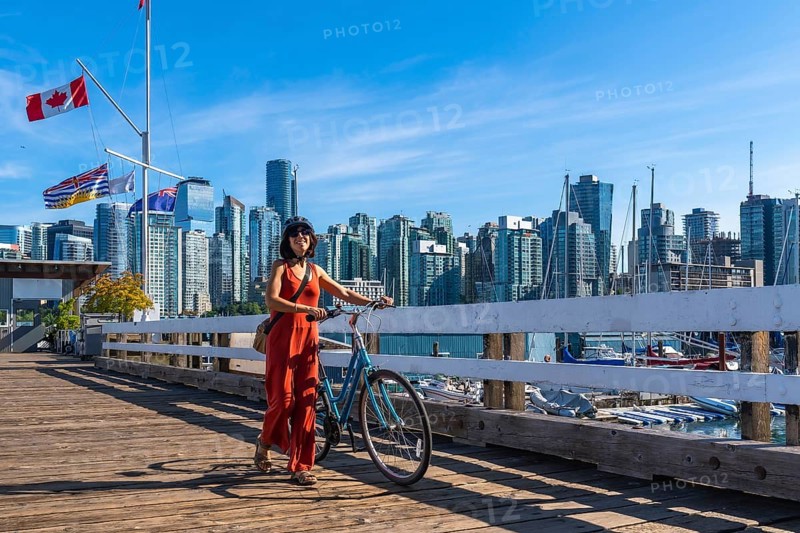Female tourist walking with her bicycle on a wooden pier, enjoying vancouver downtown skyline in british columbia, canada, on a sunny summer day