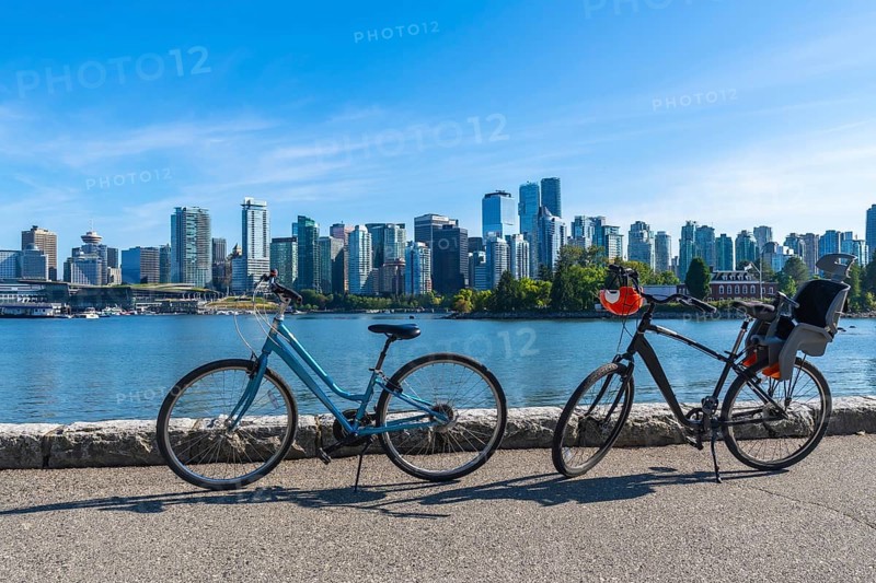 Two bicycles parked along the stanley park seawall overlook vancouver's stunning cityscape, featuring modern towers against a clear blue sky, perfect for cycling and enjoying nature