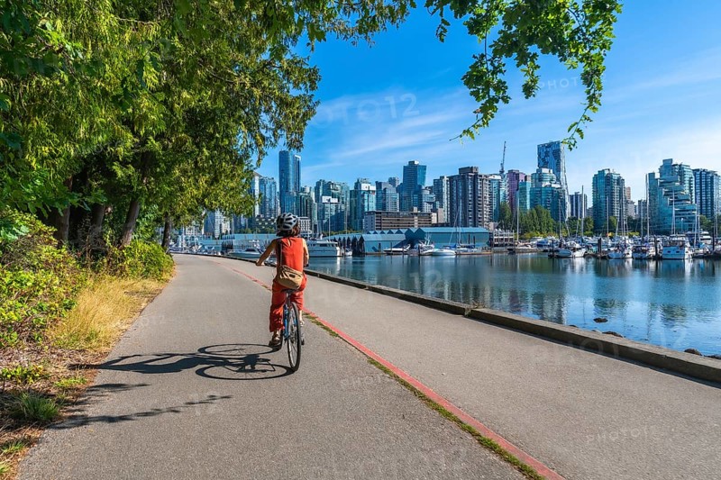 Tourist riding bicycle on the seawall in stanley park enjoying the scenic view of the vancouver skyline, british columbia, canada, on a sunny summer day
