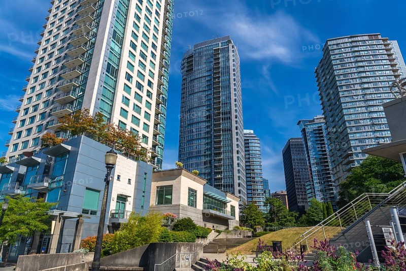 Modern skyscrapers rise above a green park in vancouver, british columbia, creating a vibrant urban landscape against a clear blue sky, showcasing the city's blend of nature and architecture