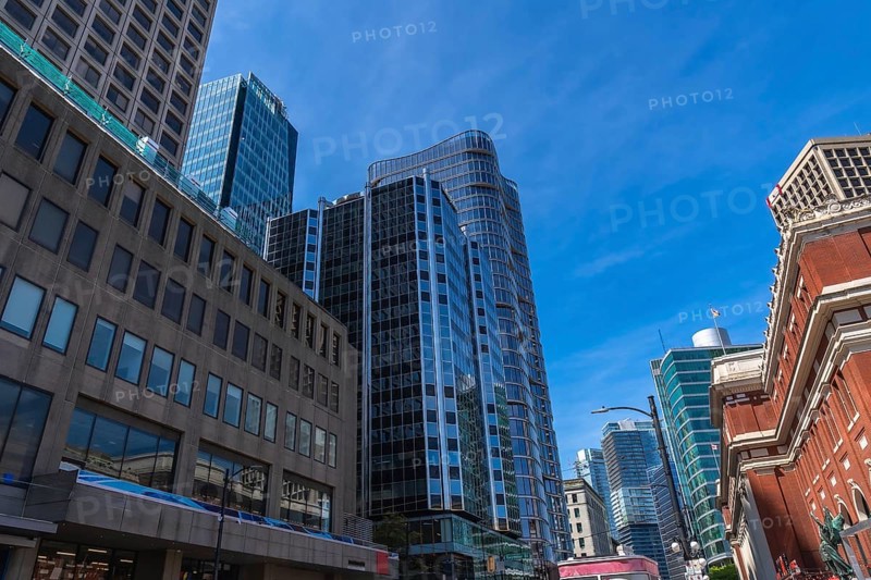 Modern glass skyscrapers and historical brick buildings stand tall against a vibrant blue sky, showcasing the architectural diversity and urban landscape of vancouver, british columbia