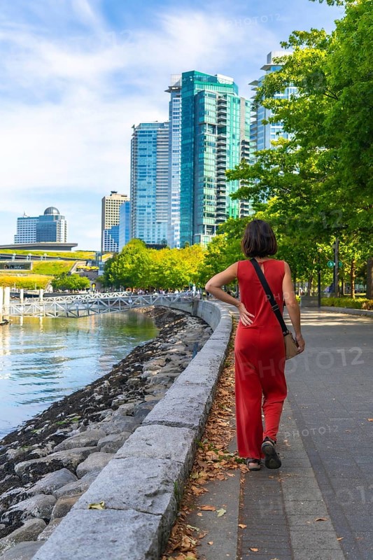 Tourist walking on the seawall in vancouver downtown with modern buildings and green trees in the background, enjoying a sunny summer day in british columbia, canada