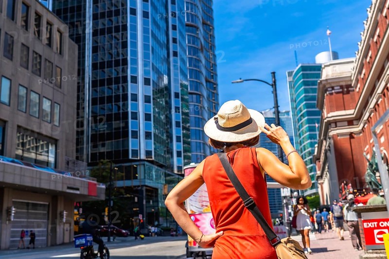 Female tourist wearing a straw hat and an orange dress is admiring the skyline of vancouver, british columbia, on a sunny summer day, enjoying the vibrant atmosphere and urban landscape