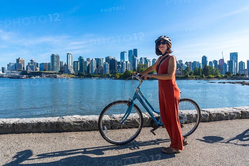 Young woman wearing a helmet stands next to her bicycle, enjoying a scenic waterfront view of vancouver's skyline in british columbia, promoting sustainable urban exploration