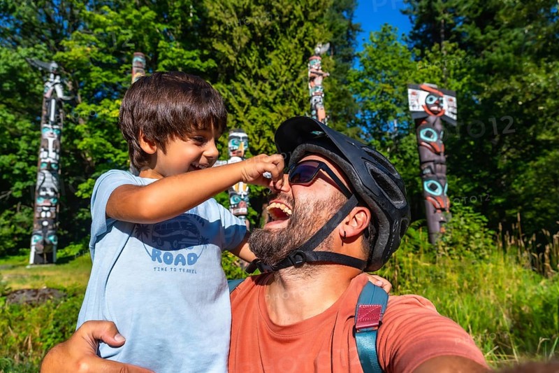 Playful father and son are enjoying a sunny day at brockton point in stanley park, vancouver, british columbia, surrounded by the iconic totem poles and lush greenery, creating a cherished memory