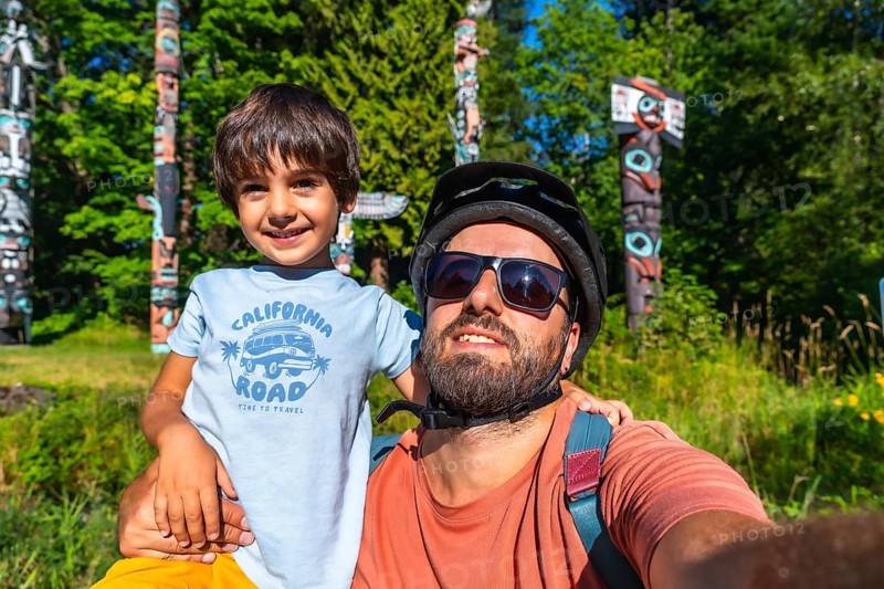 Father and son enjoying a sunny day at brockton point in stanley park, vancouver, taking a selfie with traditional totem poles in the background